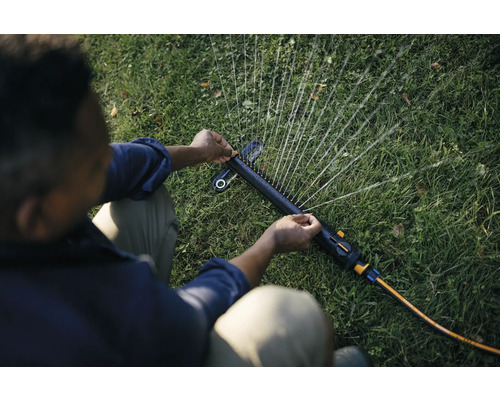 O persoană reglează un aspersor de grădină pentru a iriga gazonul.