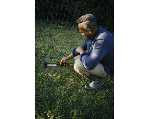 Un bărbat operează un aspersor de gazon în grădină pentru a uda iarba.