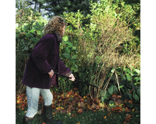 O persoană îndepărtează frunzele cu o greblă de frunze în grădină.