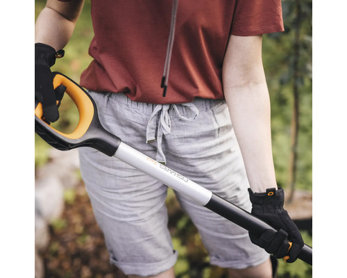 O persoană în grădină ținând o cazma cu mâner în formă de D.