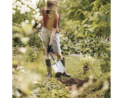 Femeie care sapă o groapă într-o grădină cu o sapă.
