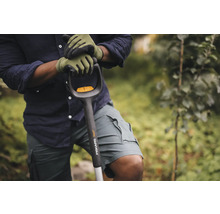 O persoană cu mănuși de grădinărit ținând o lopată Fiskars Xact.