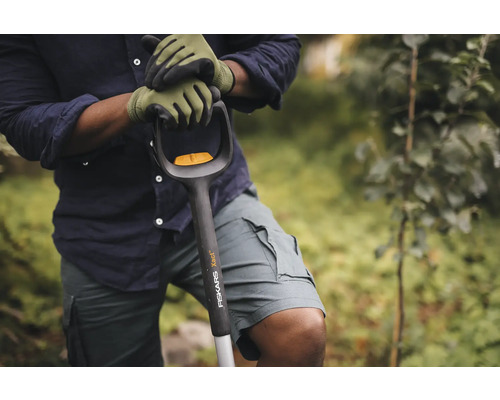 O persoană cu mănuși de grădinărit ținând o lopată Fiskars Xact.