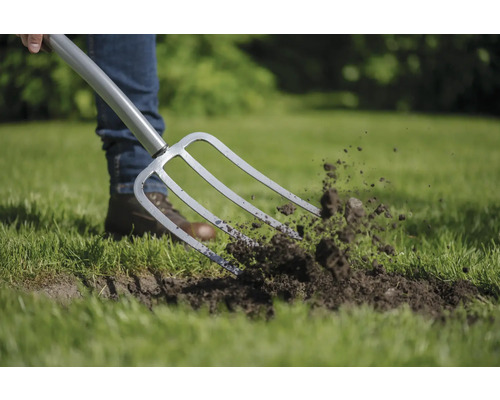 O persoană folosește o furcă de săpat pentru a grădinări pe gazon.