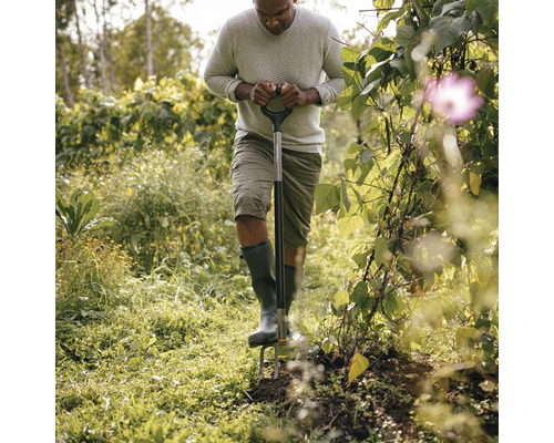O persoană folosește o furcă de săpat într-o grădină.