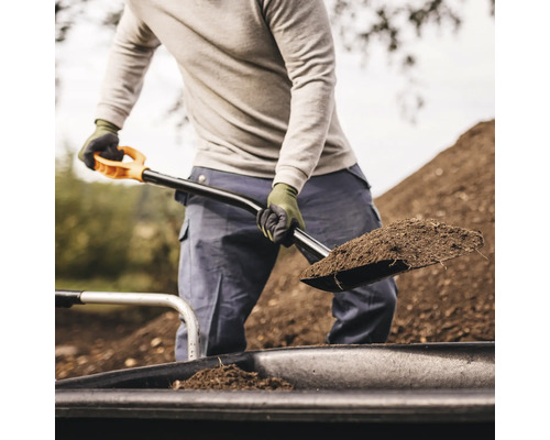 O persoană transportă pământ cu o lopată într-o roabă.