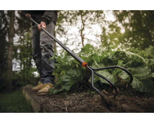 Grădinarul folosește un dispozitiv de scos buruieni Fiskars pentru a îndepărta buruienile dintr-un strat de grădină.