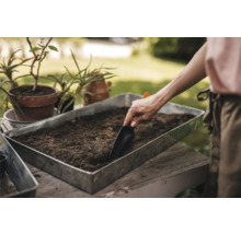 Persoană umplând un vas de plantare cu pământ cu o lopată.