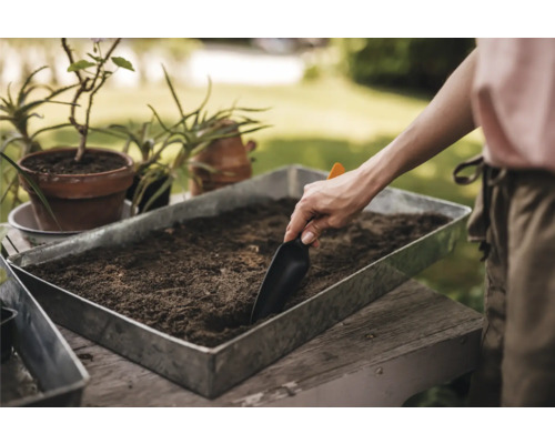 Persoană umplând un vas de plantare cu pământ cu o lopată.