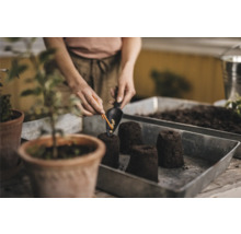 Femeie plantând răsaduri cu pământ de însămânțare și o lopată de plantare într-un vas de plantare.