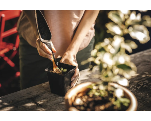 O persoană plantează o plantă cu o lopată de plantare într-un ghiveci.