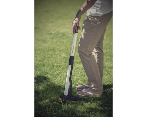 O persoană folosește un dispozitiv de scos buruieni Fiskars în grădină.