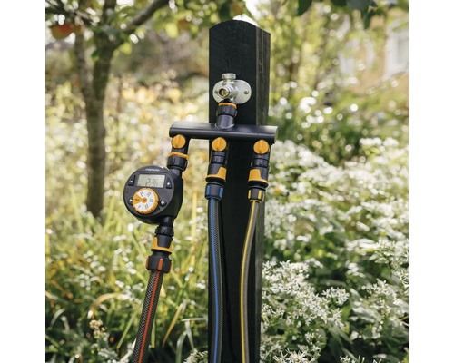 Sistem de irigare cu computer de irigare și conexiuni multiple pe un stâlp de lemn în grădină.