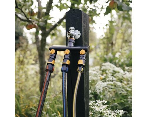 Scenă de grădină cu distribuitor de apă pe un stâlp de lemn cu furtunuri de grădină conectate