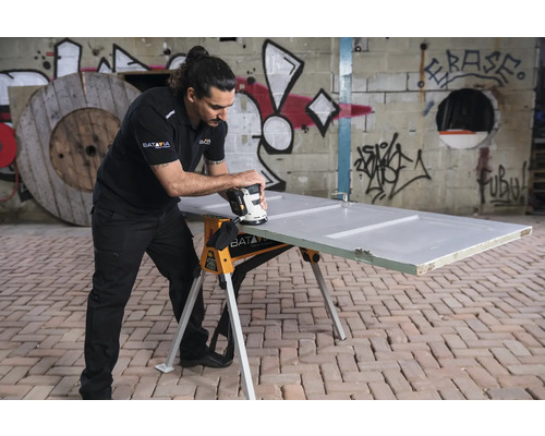 Un bărbat șlefuiește o ușă pe un suport de lucru cu o mașină de șlefuit