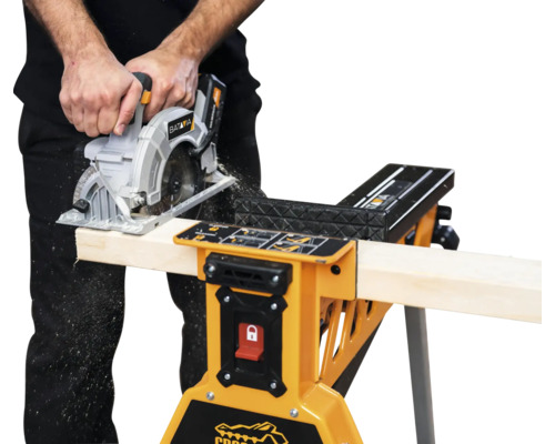 O persoană taie lemn cu un ferăstrău circular pe un banc de lucru.