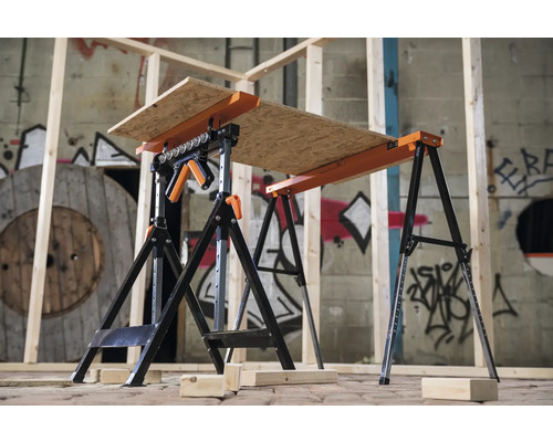 Două bancuri de lucru negre și portocalii, reglabile pe înălțime, cu o placă de lemn deasupra, se află într-o încăpere.