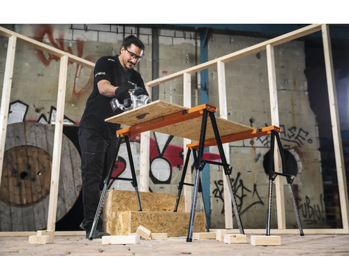 Artizan care taie o placă de lemn pe un banc de lucru cu capre duble.