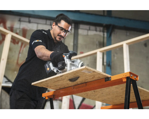 Un bărbat taie o scândură de lemn cu un ferăstrău manual pe un banc de lucru.