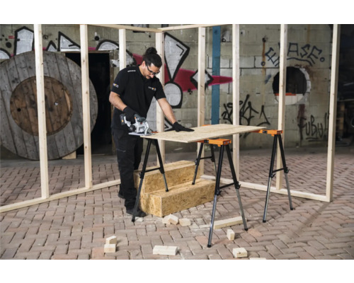 Un bărbat taie o placă de lemn pe un banc de lucru cu un ferăstrău circular