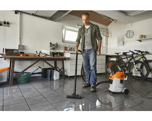 Un bărbat aspiră apă într-un garaj cu un aspirator umed uscat de la Stihl.