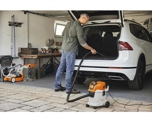 Un bărbat aspiră portbagajul unei mașini cu un aspirator umed uscat Stihl într-un garaj.