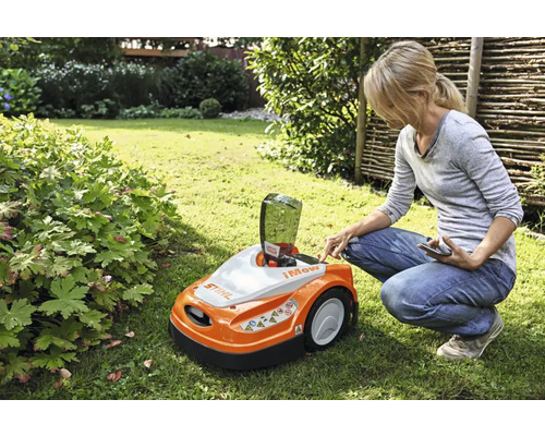 Femeie operează un robot de tuns iarba Stihl în grădină.