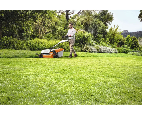 Un bărbat tunde gazonul cu o mașină de tuns iarba în grădină.