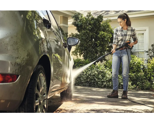Femeie curăță o mașină cu un aparat de curățat cu presiune pe o alee pavată