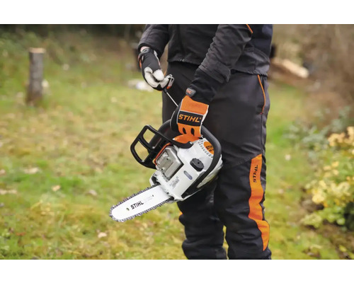 O persoană ține un ferăstrău cu lanț Stihl afară. Ferăstrăul cu lanț și îmbrăcămintea de lucru sunt marca Stihl.