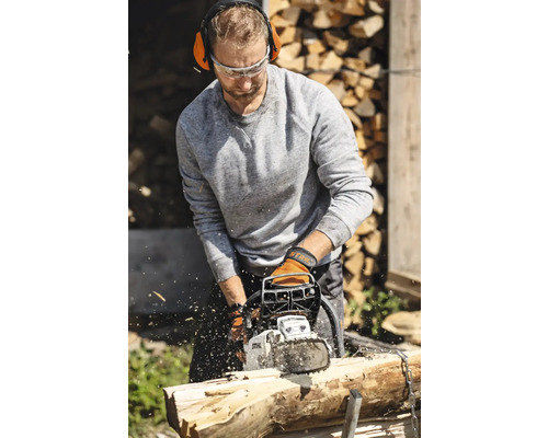 Bărbat taie lemne cu un motoferăstrău, echipat cu protecție auditivă și ochelari de protecție.