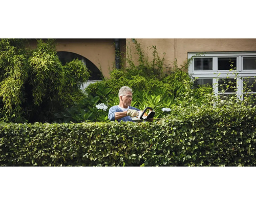 Un bărbat taie un gard viu cu o foarfecă de tuns gard viu în grădină.