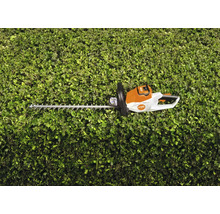 Foarfecă de tuns gard viu cu acumulator STIHL în fața unui gard viu verde