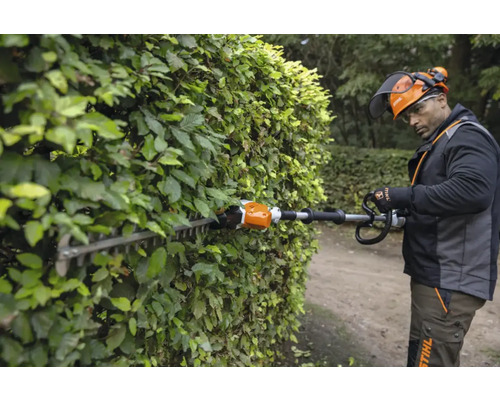 O persoană taie un gard viu cu o foarfecă de tuns gard viu.