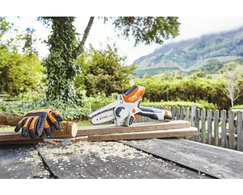 Fierăstrău cu lanț cu acumulator cu mănuși de protecție pe masă de lemn în grădină