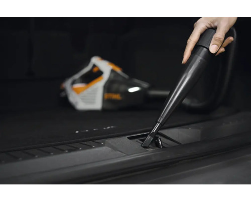 O persoană folosește un aspirator portabil fără fir Stihl pentru a curăța interiorul unei mașini.