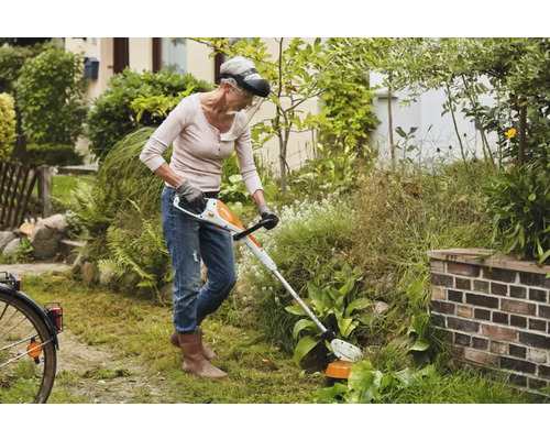 Femeie lucrând cu o mașină de tuns iarba cu acumulator în grădină.