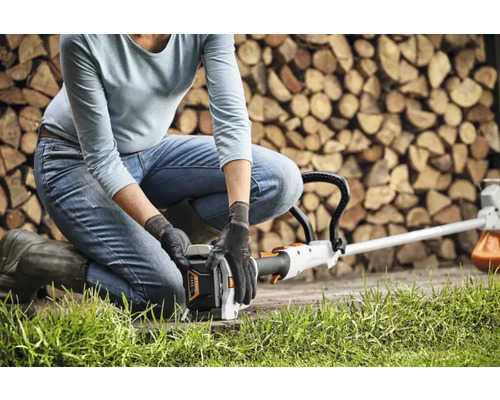 O persoană se ghemuiește pentru a opera o mașină de tuns iarba în fața unei stive de lemne de foc.