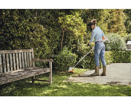 O femeie tunde iarba cu o mașină de tuns iarba într-o grădină.