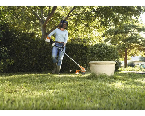 O femeie operează o mașină de tuns iarba în grădină.