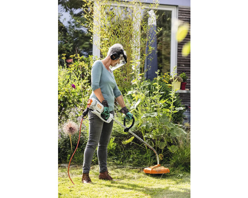 O femeie folosește o mașină de tuns iarba în grădină pentru îngrijirea gazonului