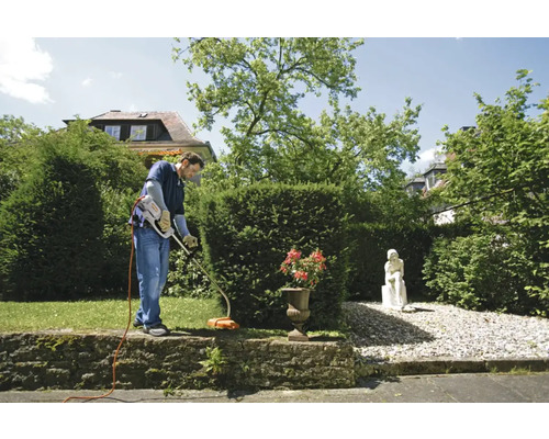 Bărbat tunde iarba cu o mașină de tuns iarba în grădină.