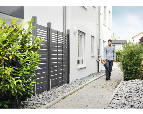 Un bărbat folosește o suflantă de frunze de-a lungul unui gard din grădină.