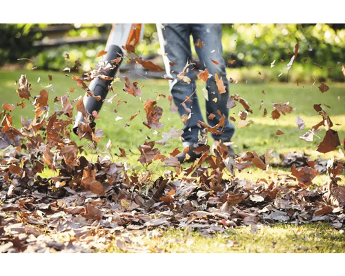 Persoană care folosește o suflantă de frunze în grădină pentru a îndepărta frunzele