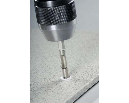 O mașină de găurit forează o gaură într-o placă de faianță cu un burghiu pentru faianță