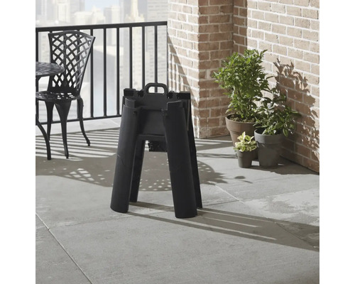 Capră de tăiere neagră pliată pe un balcon cu un perete de cărămidă și plante