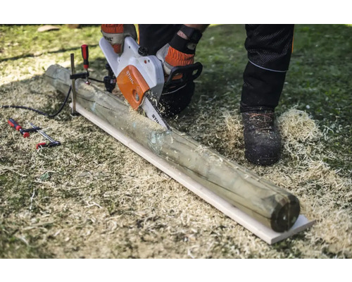 O persoană taie cu un motoferăstrău un stâlp de lemn, care este fixat cu o clemă.