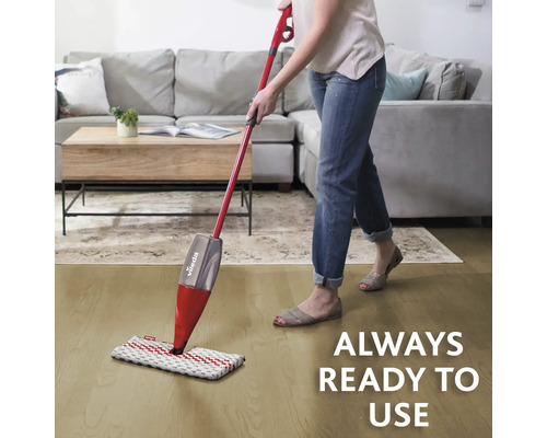 Femeie șterge podeaua cu un mop Vileda în fața unei canapele