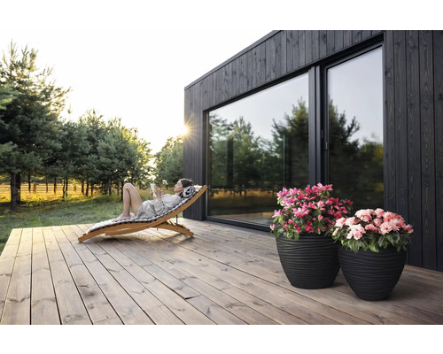 "Scenă cu o femeie care se relaxează pe un șezlong din lemn pe o terasă din lemn în fața unei case cu ferestre mari