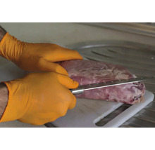 O persoană cu mănuși taie carne cu un cuțit pe un tocător.